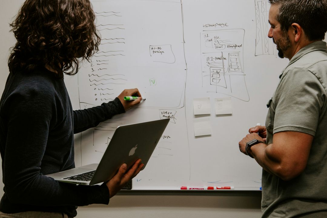 Two colleagues mapping out ideas at a whiteboard, one holding a laptop